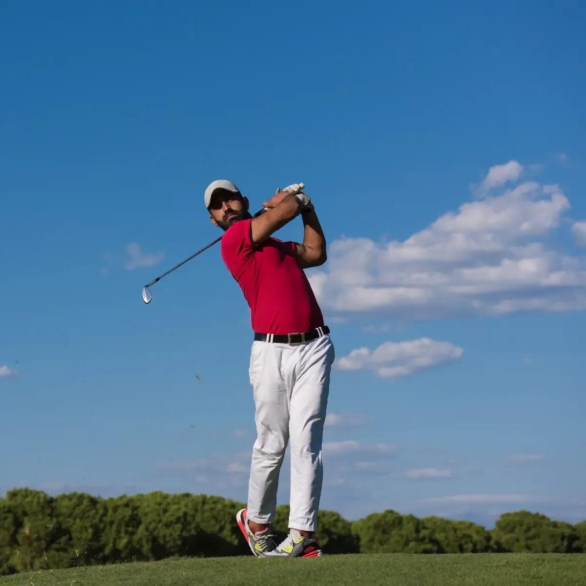 masters golf pool golfer swinging a club on a clear blue-sky course.