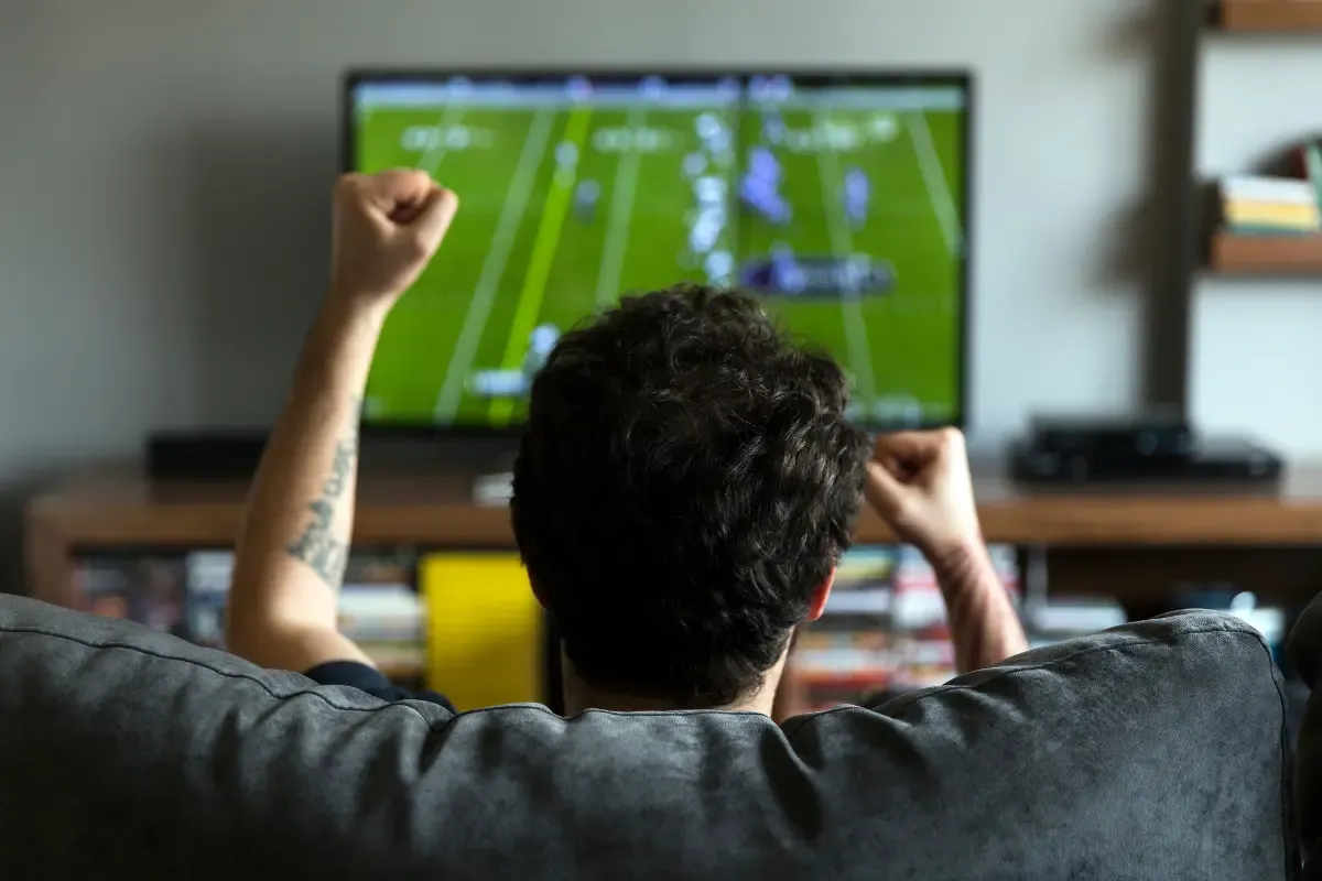 NFL Pick Strategy fan cheering on a couch while watching a football game on television.