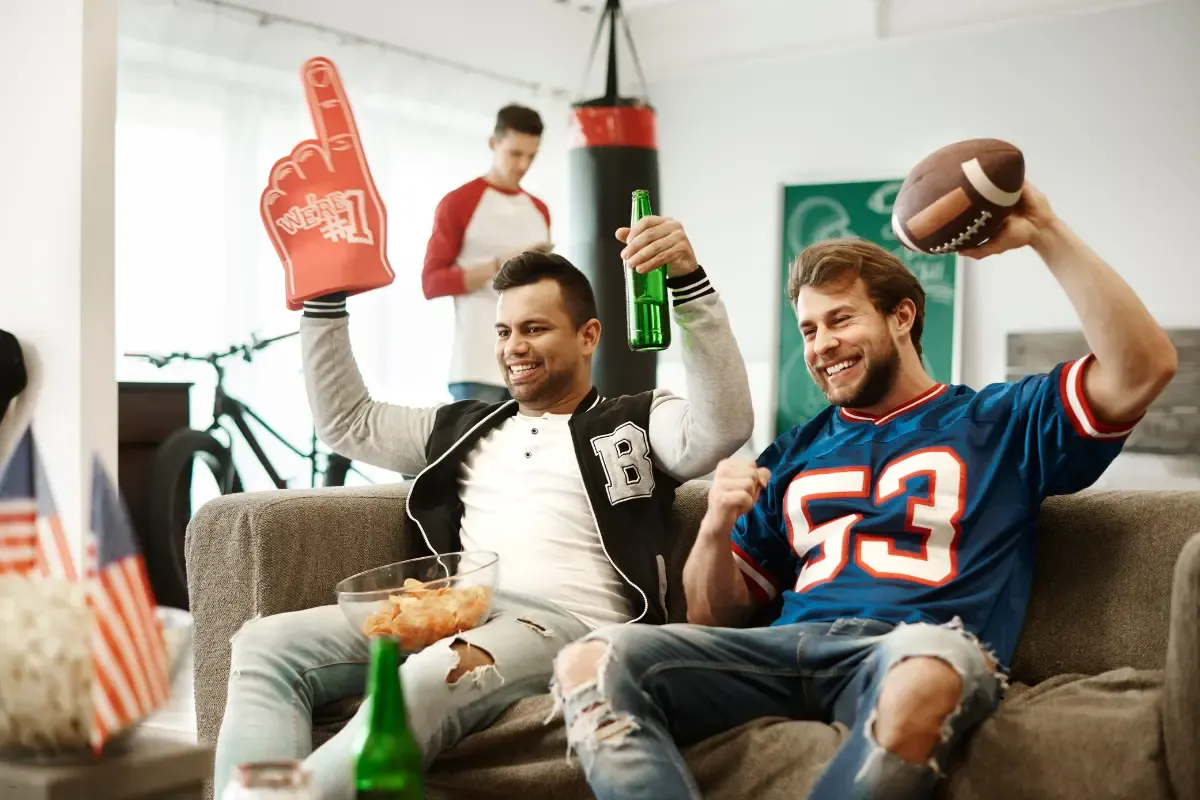 Peer-to-peer contest platforms as two excited friends cheer while watching a football game at home.