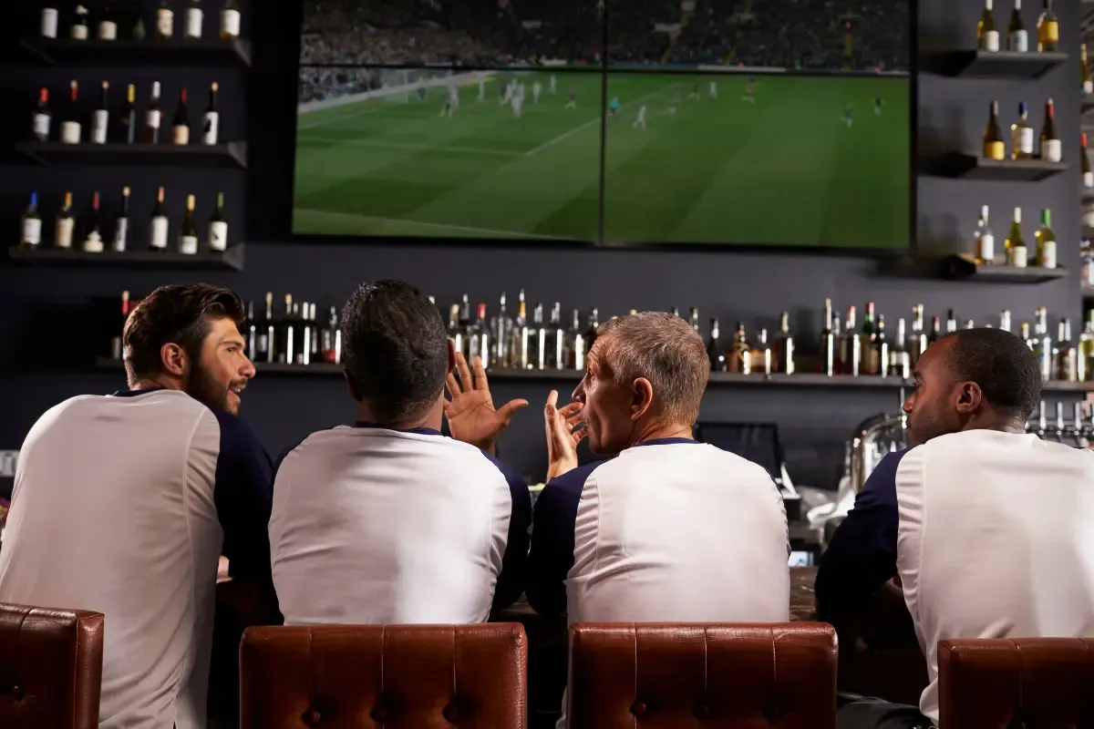 Fantasy football picks as sports fans discuss plays while watching a game at a bar with multiple screens.