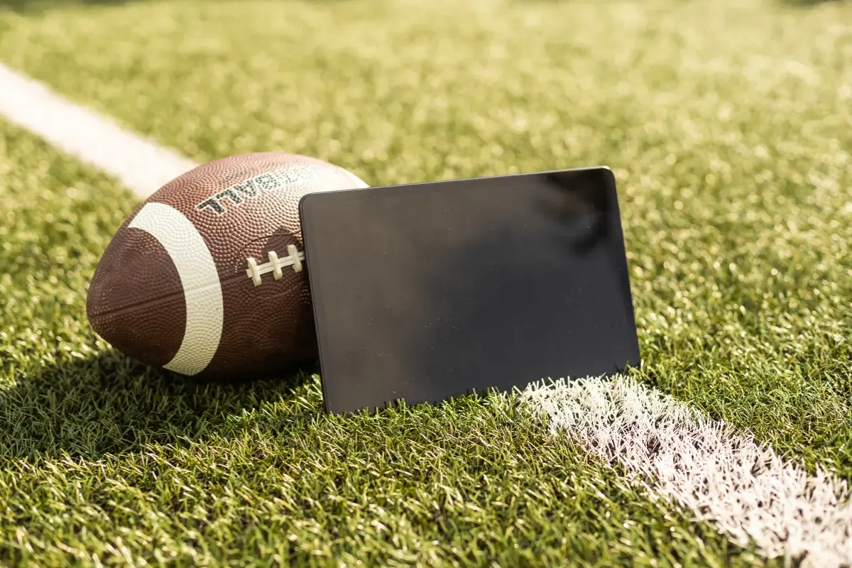 Football and tablet lying on a football field’s white line, representing sports and technology