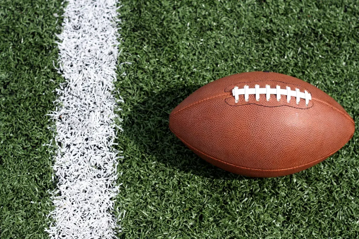 Football lying on a field next to a white line, ready for play
