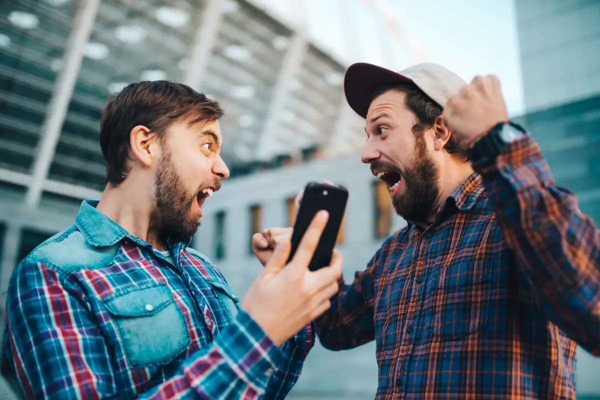 Two friends cheering enthusiastically while looking at a smartphone, standing outside a stadium