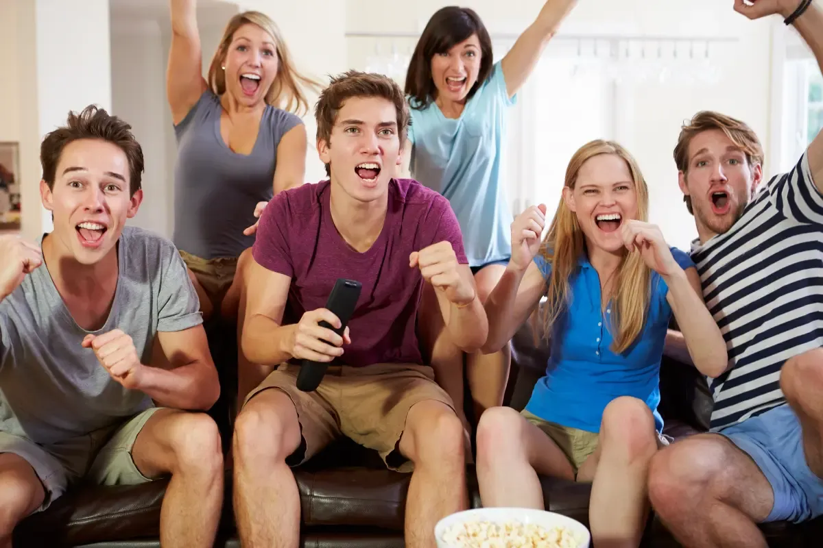 Group of friends enthusiastically cheering while watching TV in a cozy home setting