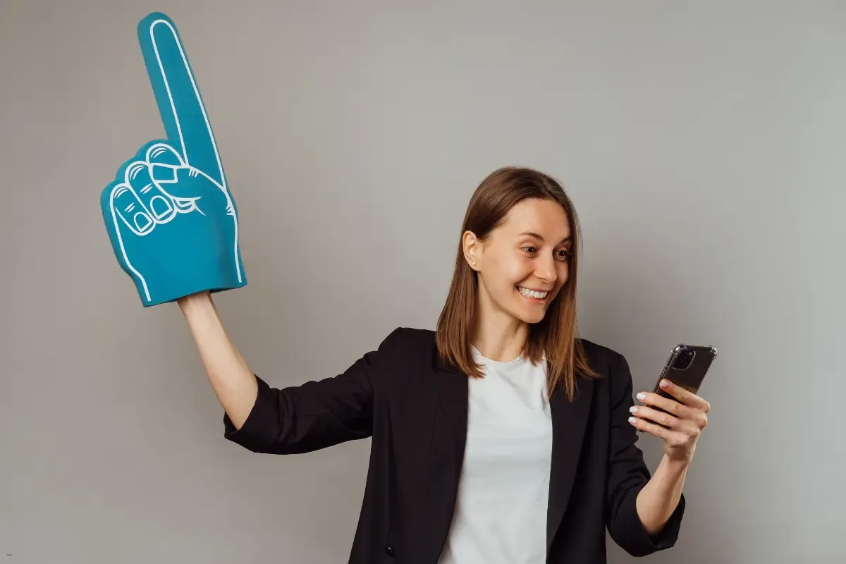 Woman celebrates holding a foam finger and a phone while looking at DFS website