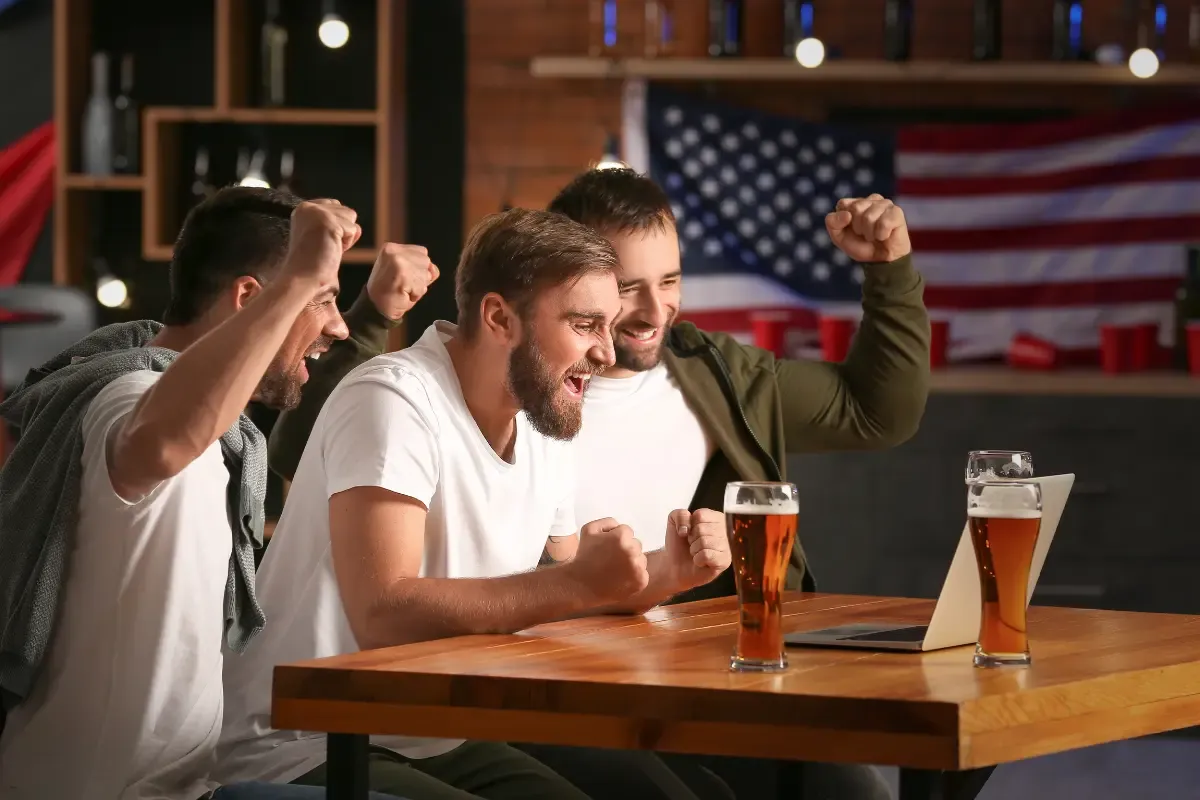 Friends celebrating NFL daily fantasy wins while watching a game on a laptop at a bar