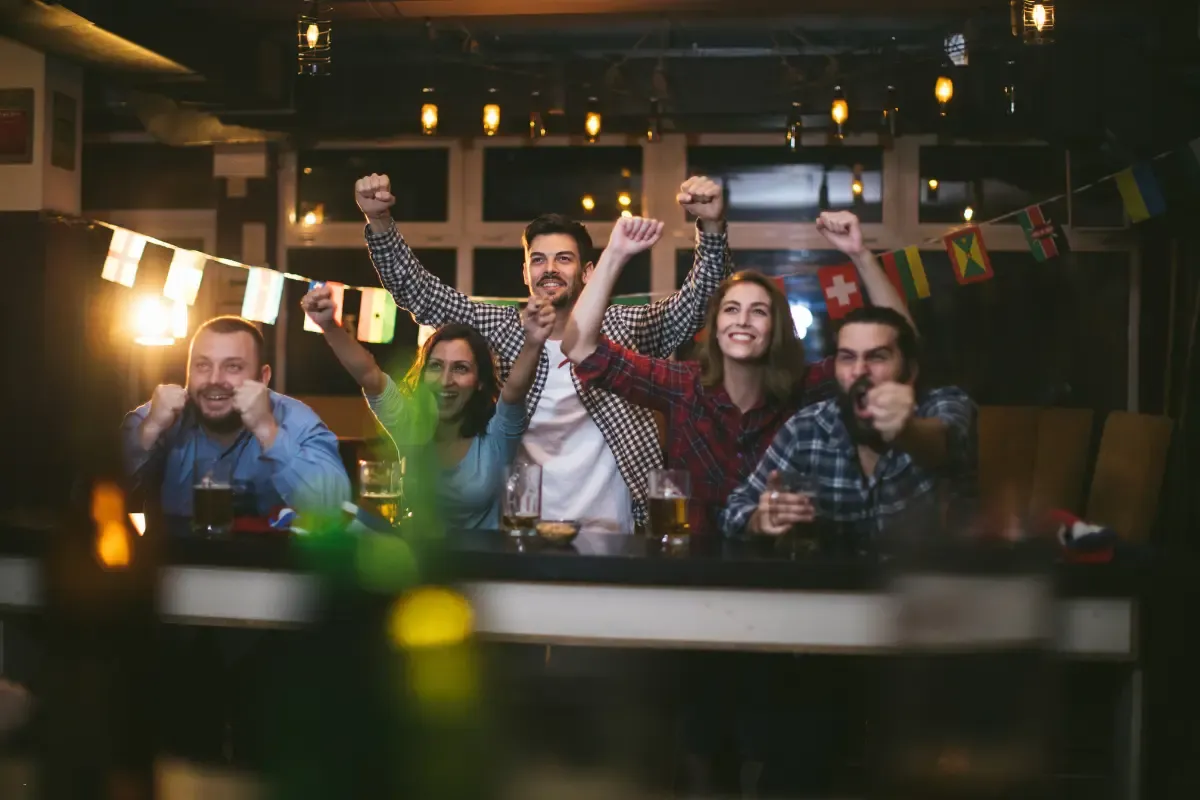 Group of NFL daily fantasy enthusiasts cheering in a bar with international flags and drinks in the background