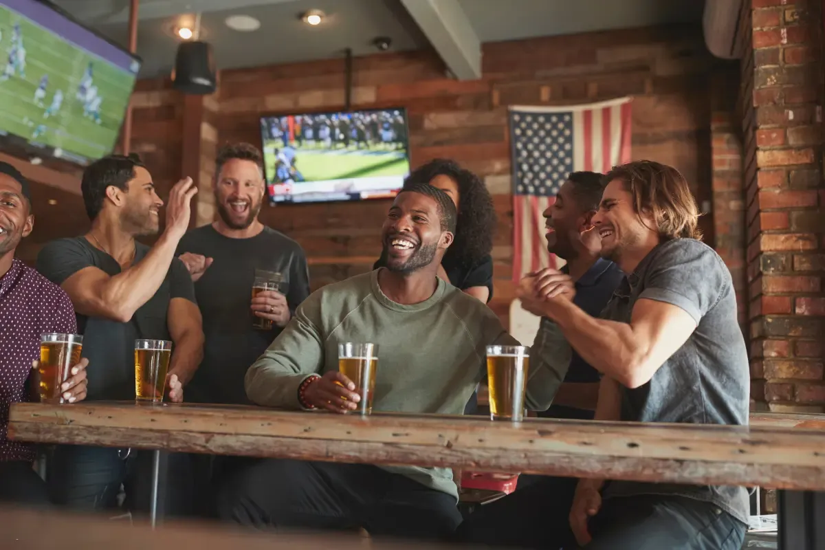 NFL daily fantasy players laughing and enjoying drinks while watching a football game in a lively sports bar