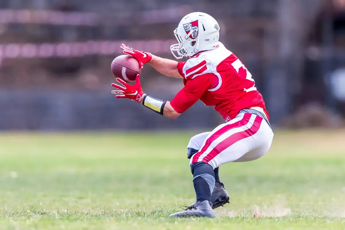 College football player in a red uniform preparing to catch the ball during a live game on the field