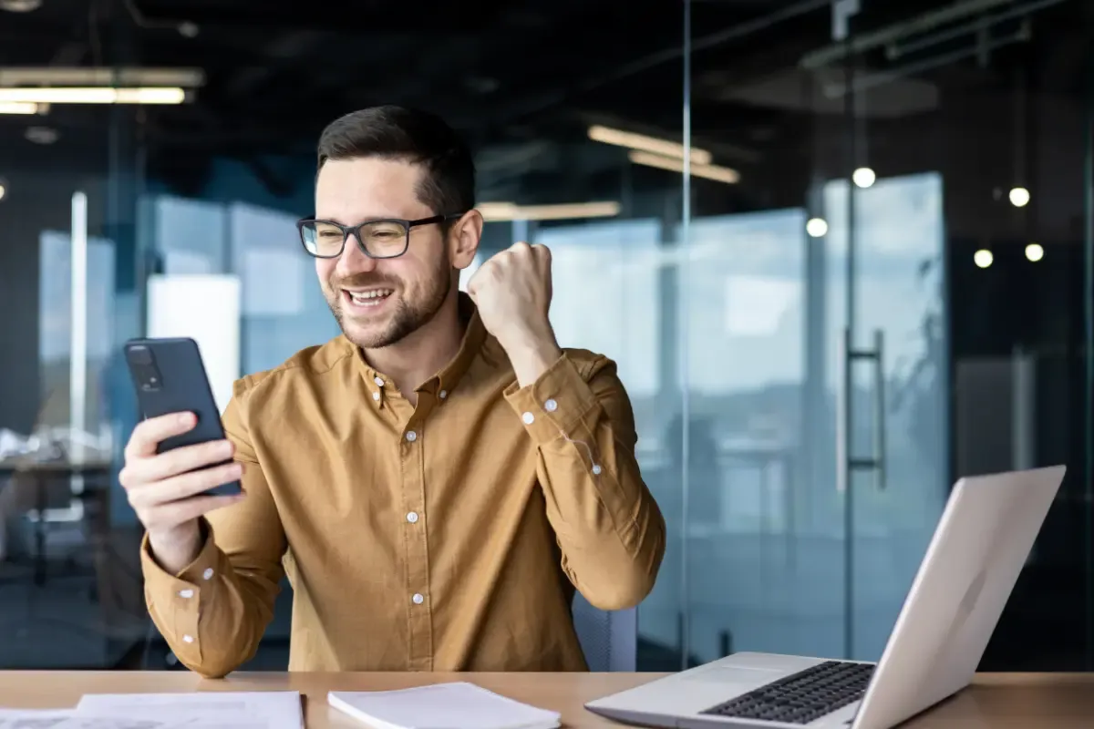 Survivor pool app user celebrating a win while checking scores on a smartphone at an office desk