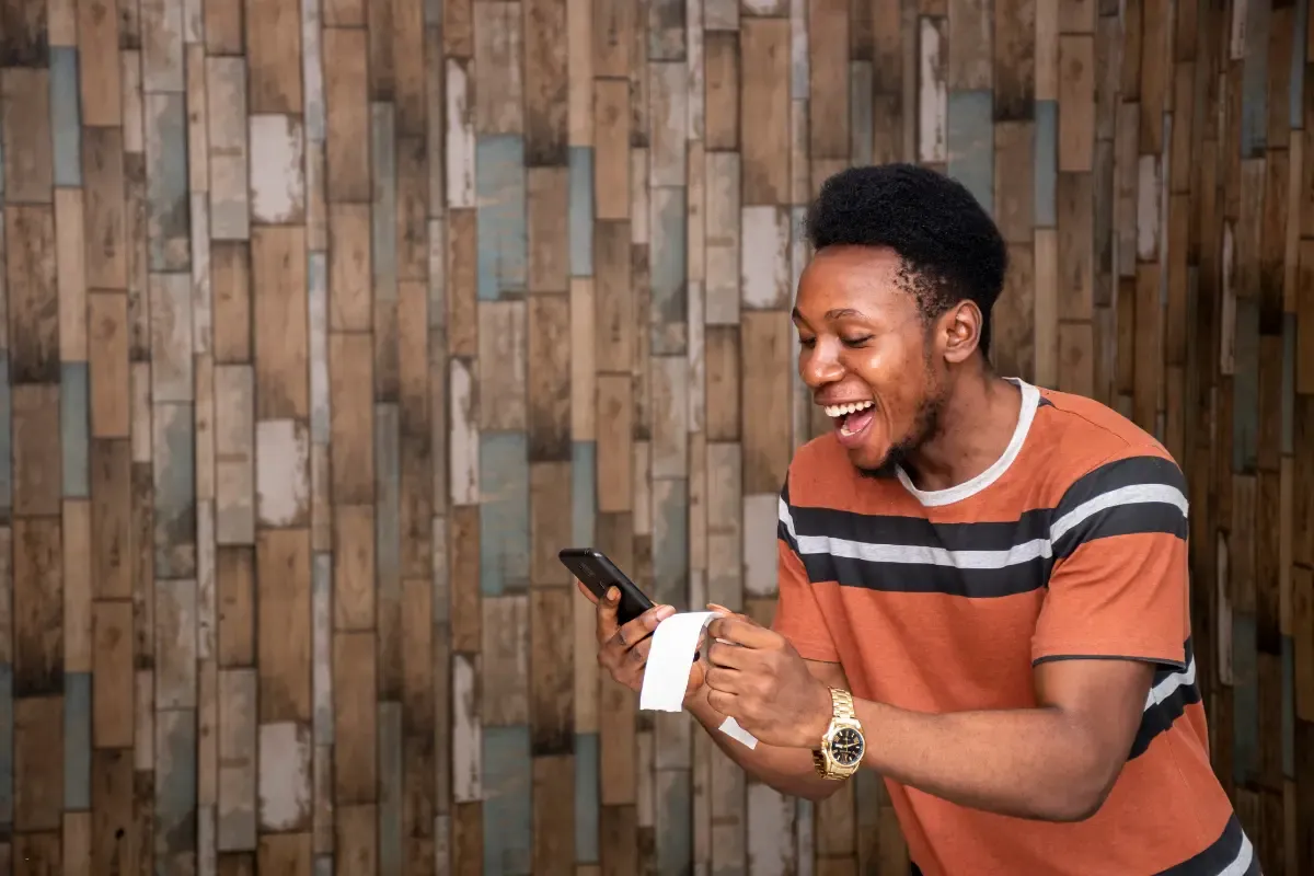 Online site for sports contests user celebrating while checking results on a smartphone and holding a receipt