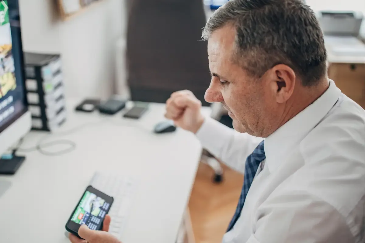 Survivor pool website participant tracking game results on a smartphone while sitting at a workstation