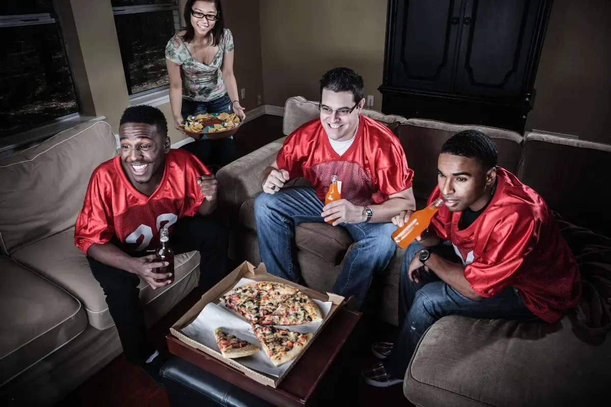 NFL survivor pool fans in red jerseys watching a football game with pizza and drinks at home