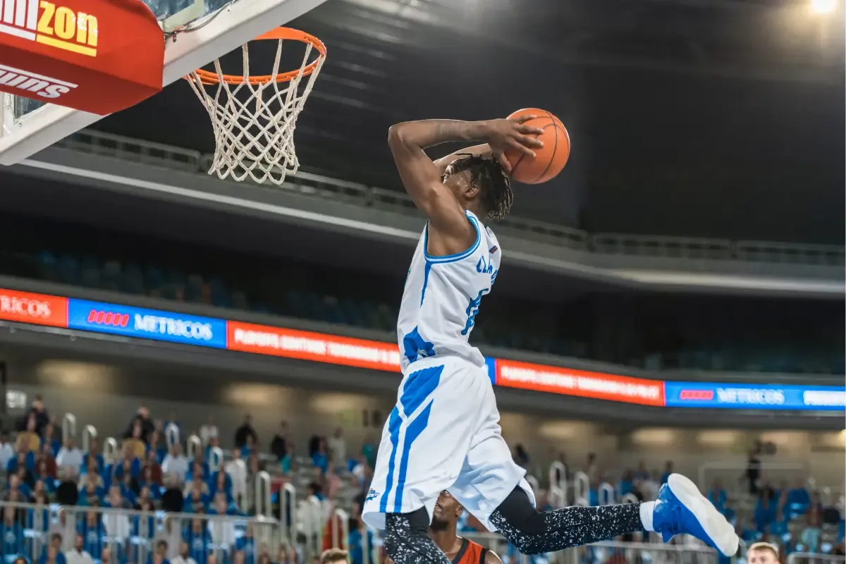 March Madness fantasy basketball action as a player in a blue jersey jumps for a slam dunk during a game