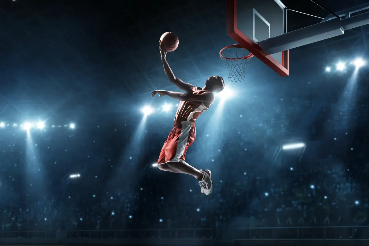 March Madness pool player in red jersey soaring towards the basket in a packed arena under bright lights