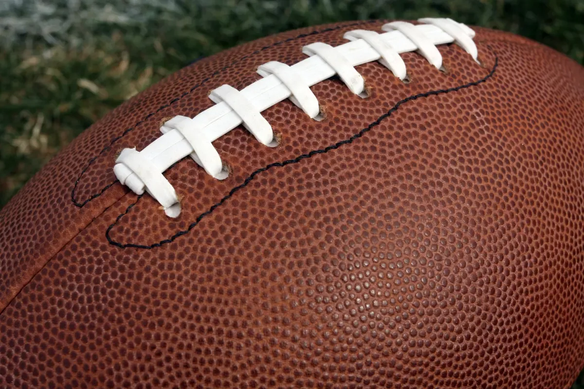 NFL daily fantasy sports close-up of a textured football with white laces on a grassy field background