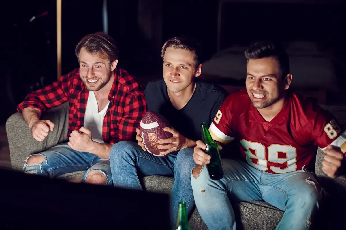 NFL daily fantasy sports group of friends watching a football game, one holding a football while others cheer.