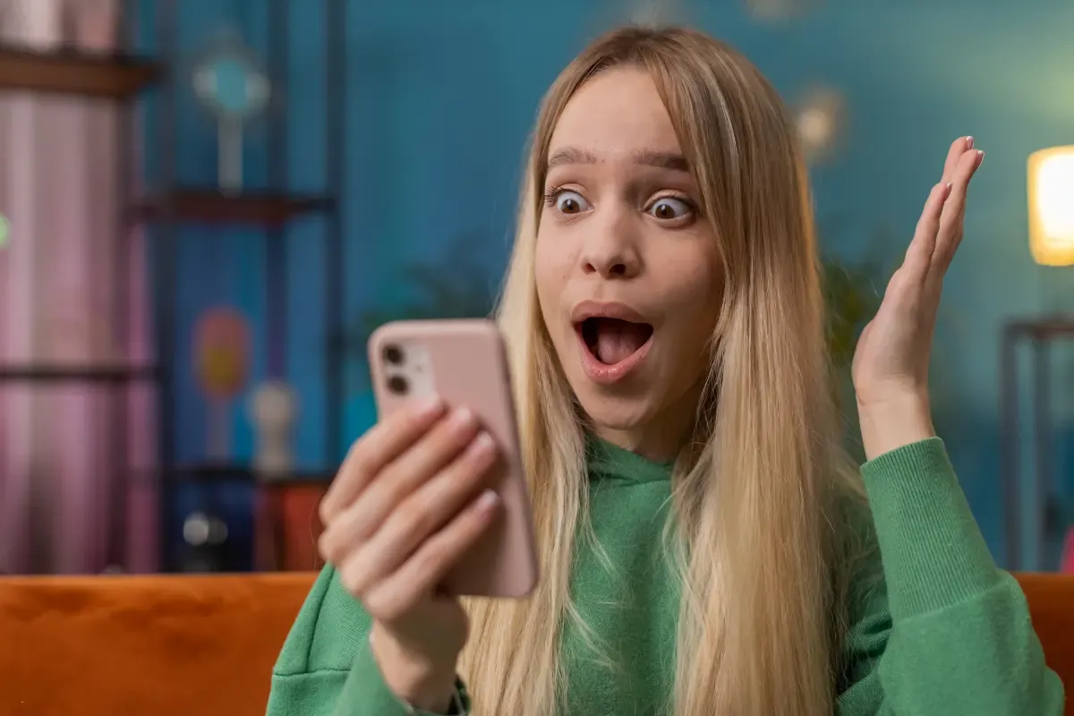 Surprised young woman in a green hoodie reacting to something on her smartphone in a colorful room
