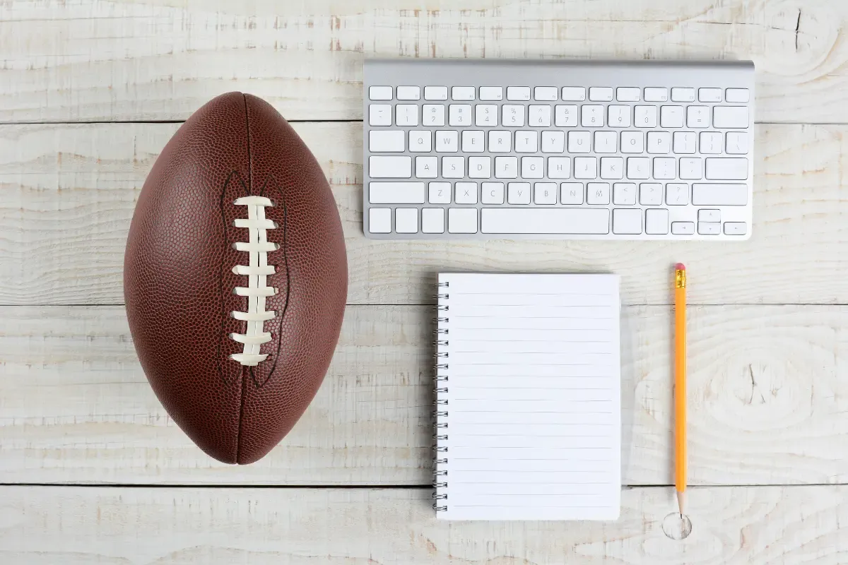 Football placed on a wooden desk next to a keyboard, notebook, and pencil.