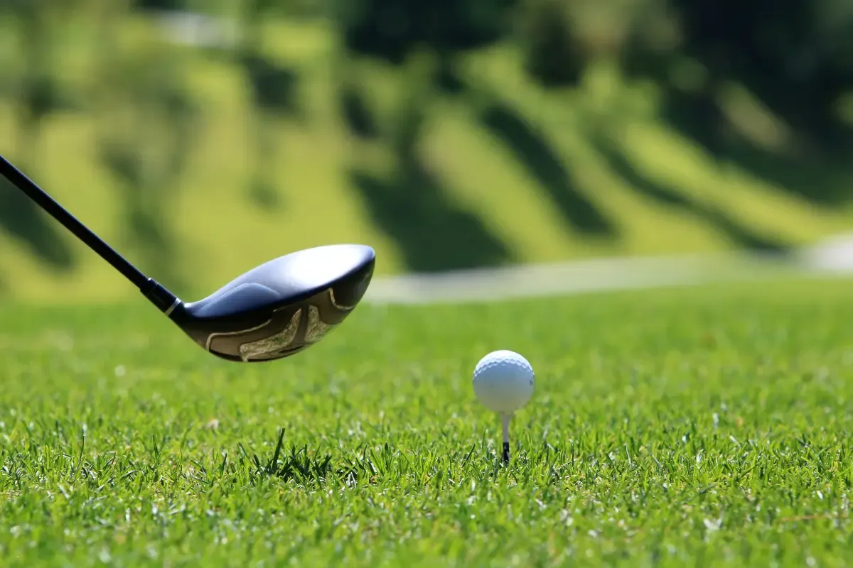 A golf club preparing to strike a golf ball on a tee with a blurred fairway in the background
