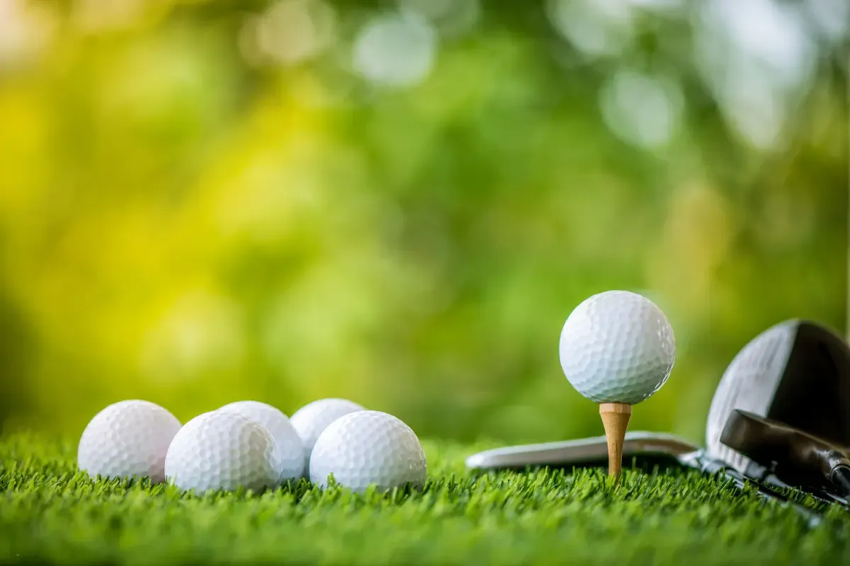 A golf ball on a wooden tee with additional balls and clubs on lush green grass.
