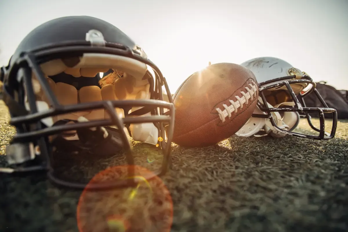NFL survivor pool strategies symbolized by a football and helmets lying on the field at sunset.