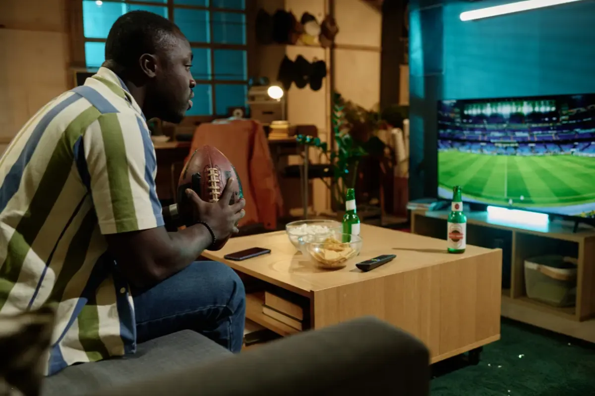 Navigating NFL matchups depicted by a fan intensely watching a football game on TV while holding a football.
