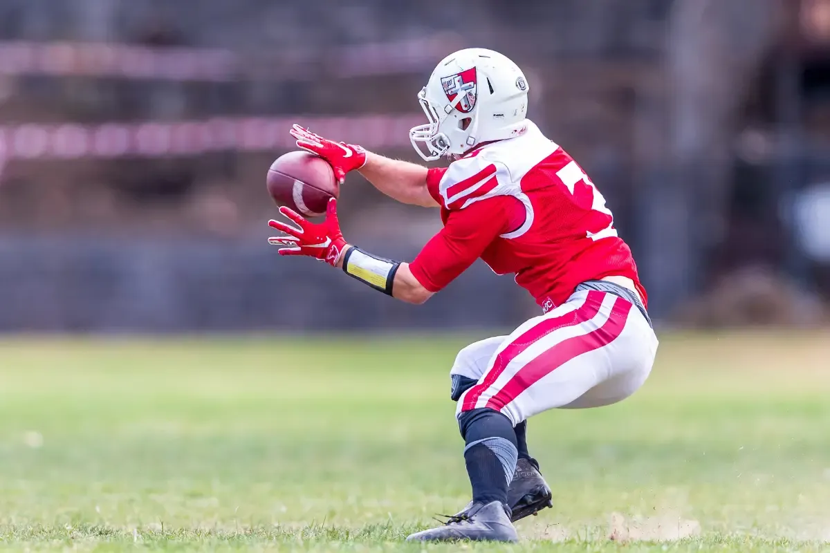 NFL strategy models illustrated by a football player crouching to catch a pass during a daytime game.