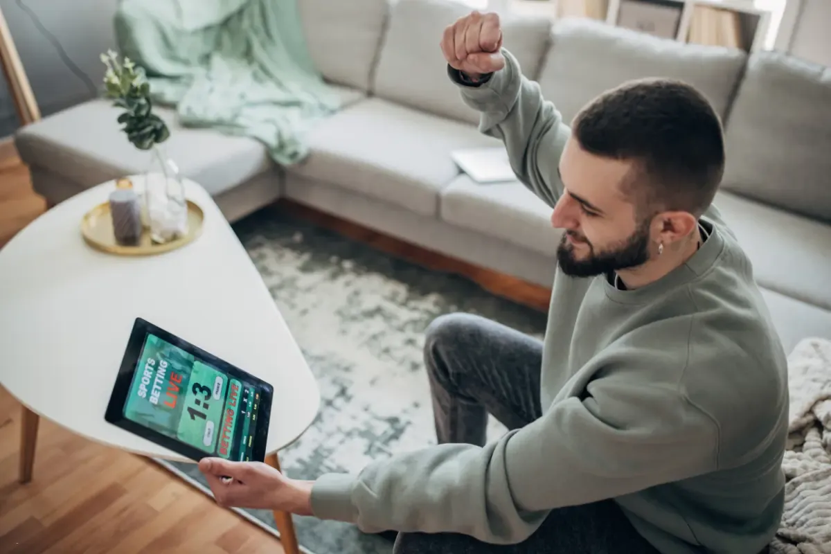 NFL pick’em website excitement captured as a man cheers while checking live sports betting scores on a tablet.