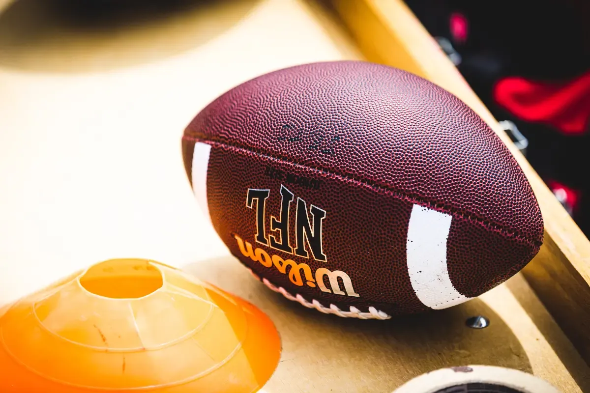 Advanced NFL stats concept shown with a close-up of a Wilson NFL football beside training cones on a bench.