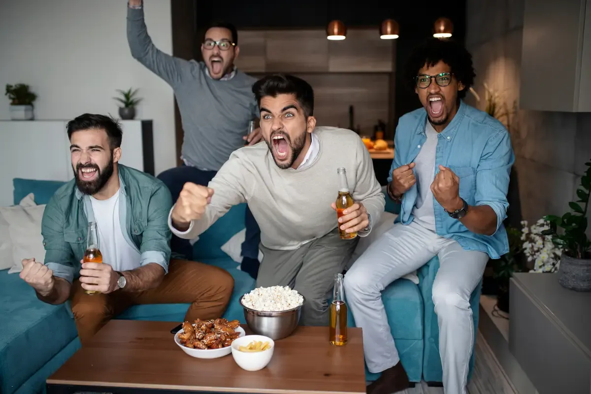 NFL fantasy sleepers excitement shown by four friends cheering with beer and snacks during a football game.