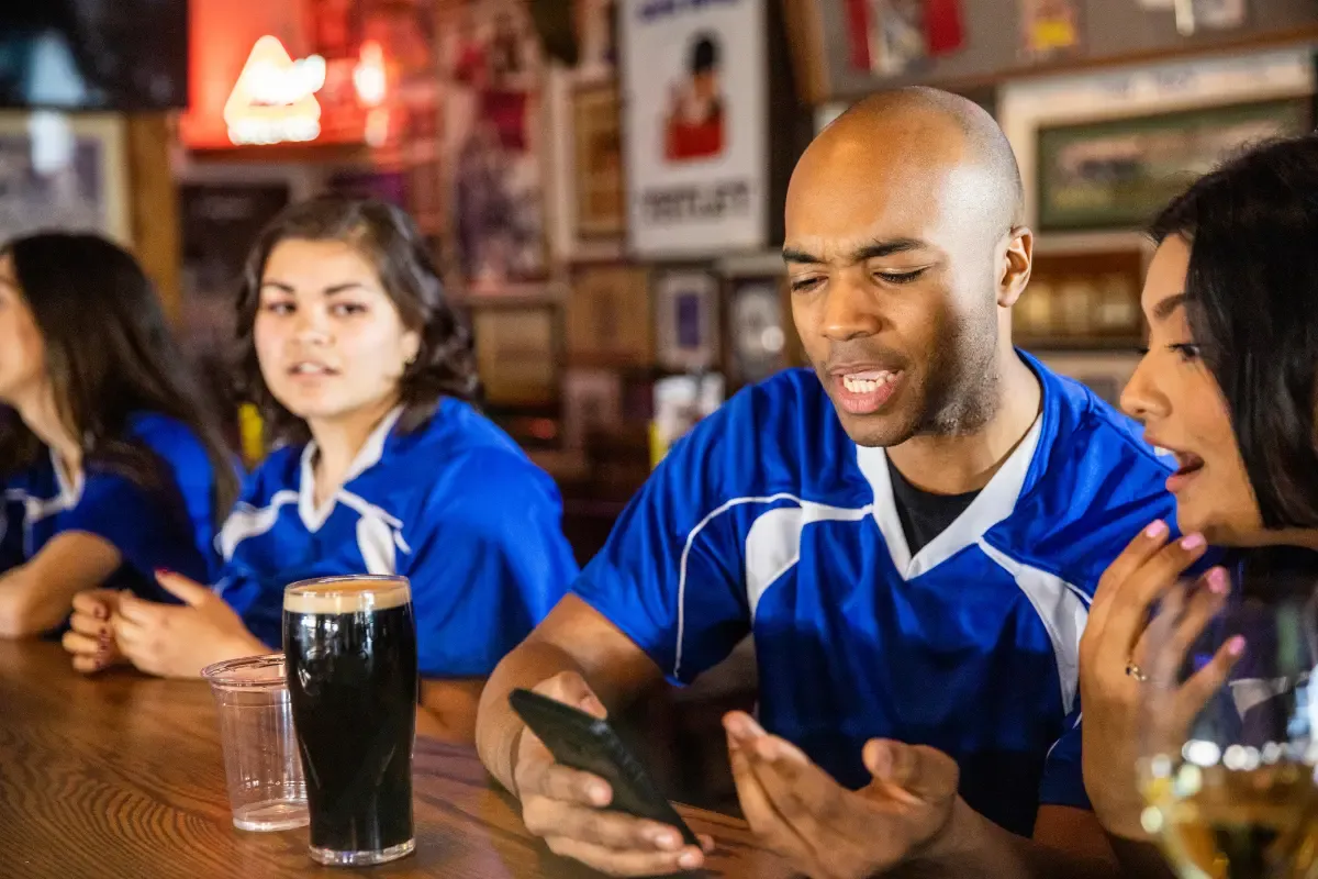 Fantasy sports strategy discussed by friends in team jerseys at a sports bar while checking a phone.