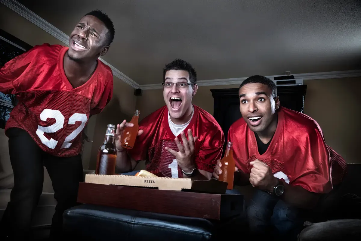 NFL fantasy football pick'em players in jerseys reacting to a game with pizza and soda bottles.