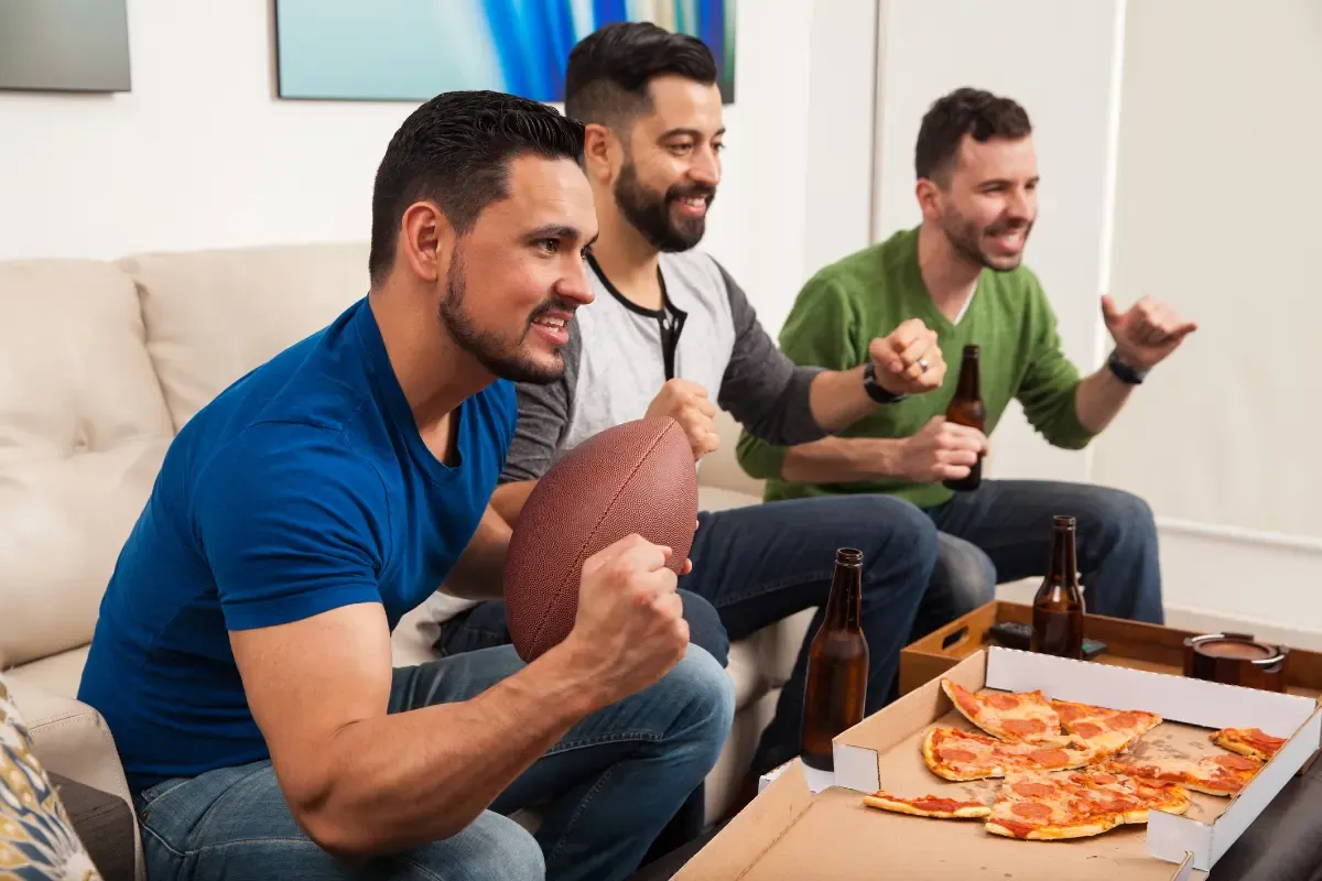 NFL pick'em fantasy fans intensely watching a game on TV with pizza and drinks on the table