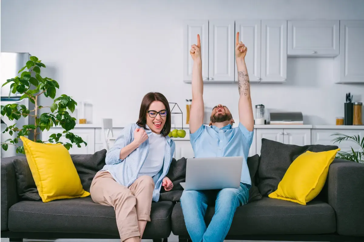 NFL tiers pool success sparks celebration for couple cheering in front of laptop on living room couch
