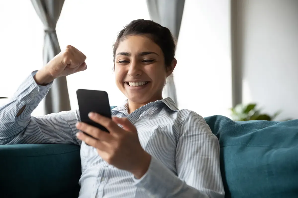 Fantasy football pool winner celebrates joyfully while checking results on smartphone at home.