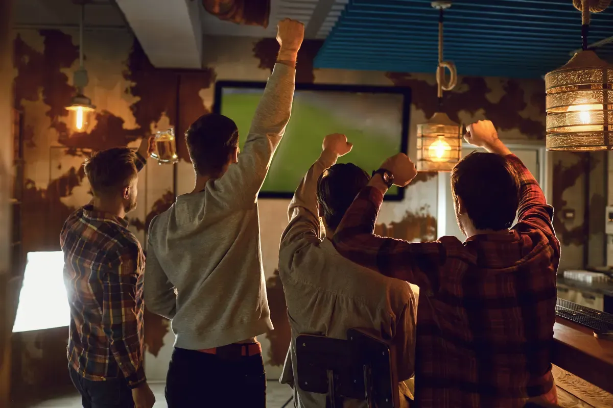 Survivor football pool fans cheer in a rustic bar setting while watching a game on a big screen