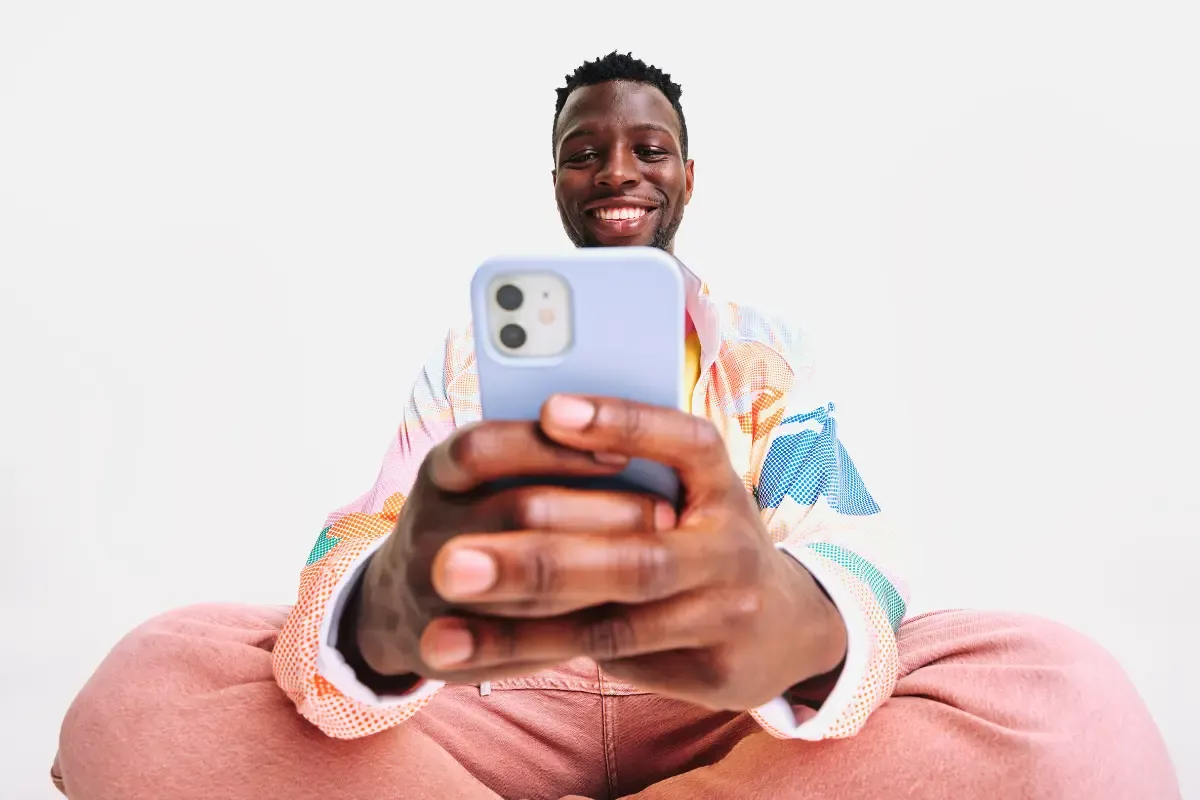 NFL survivor pool player smiles while using a smartphone in a colorful outfit against a plain background