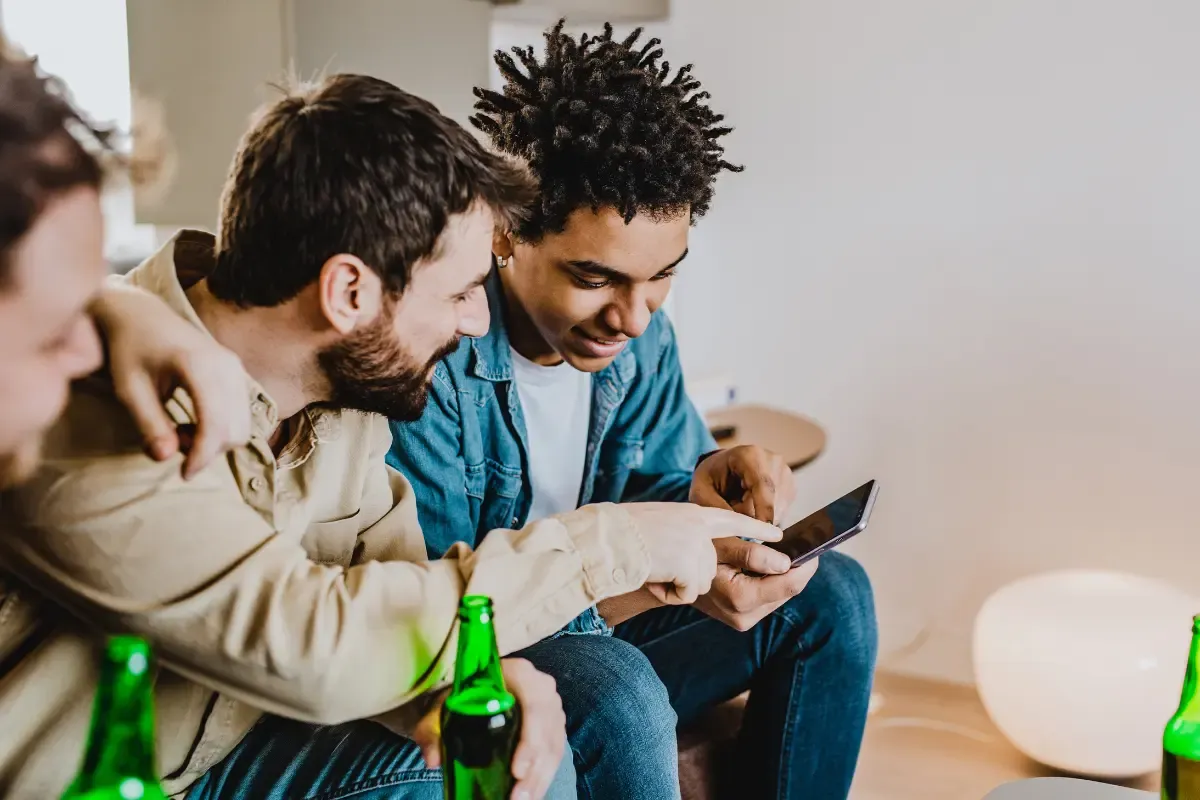 NFL pool strategy discussion between friends reviewing picks on a smartphone while relaxing with drinks at home.