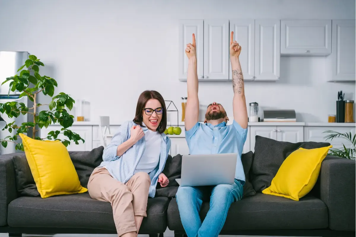 NFL confidence pool participants celebrating a winning pick while watching a game on a laptop at home.