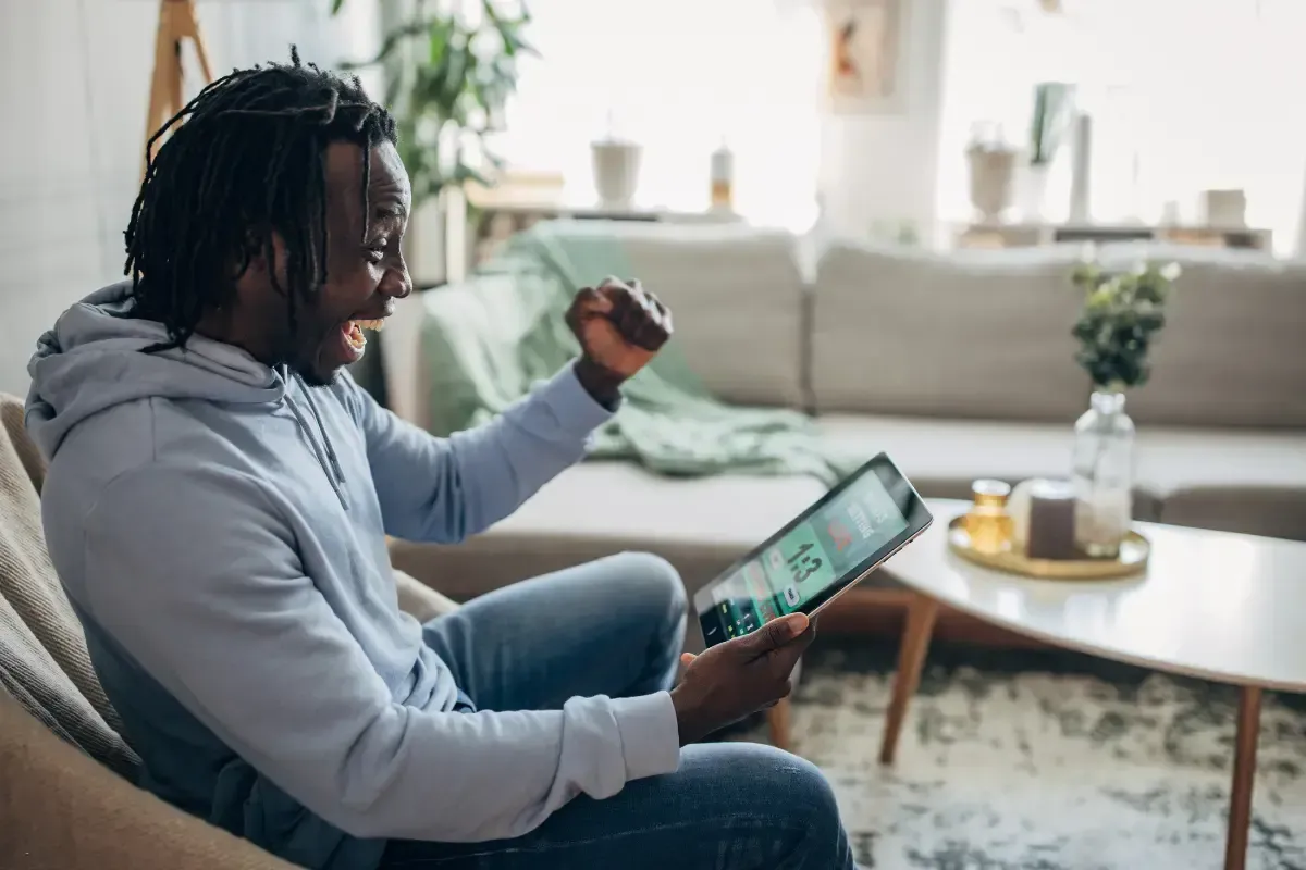Survivor football pool fan celebrates winning pick on tablet in a cozy living room.