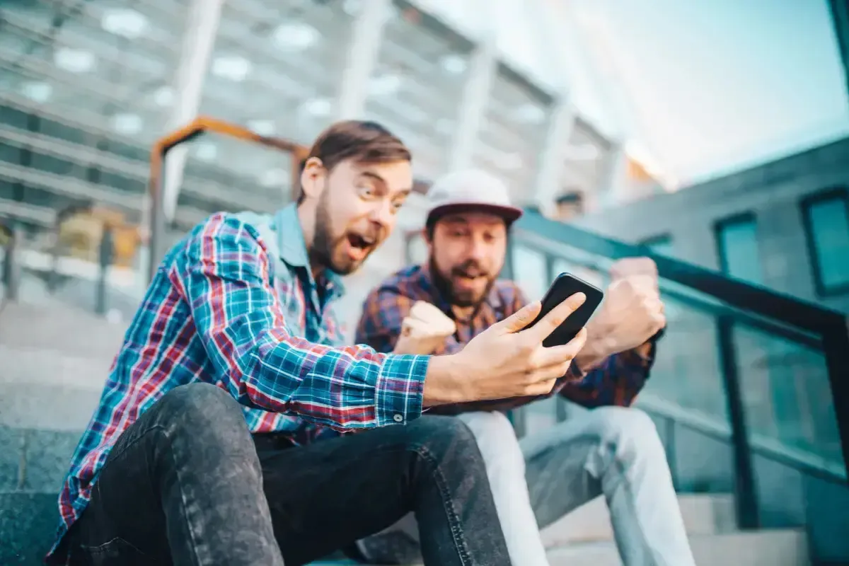 Fantasy golf advice leads to celebration as two friends check their picks on a smartphone outside a building.