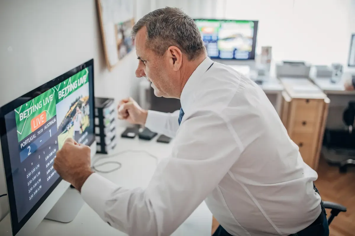 Online NFL betting excitement as a man celebrates while watching live odds on a computer screen.
