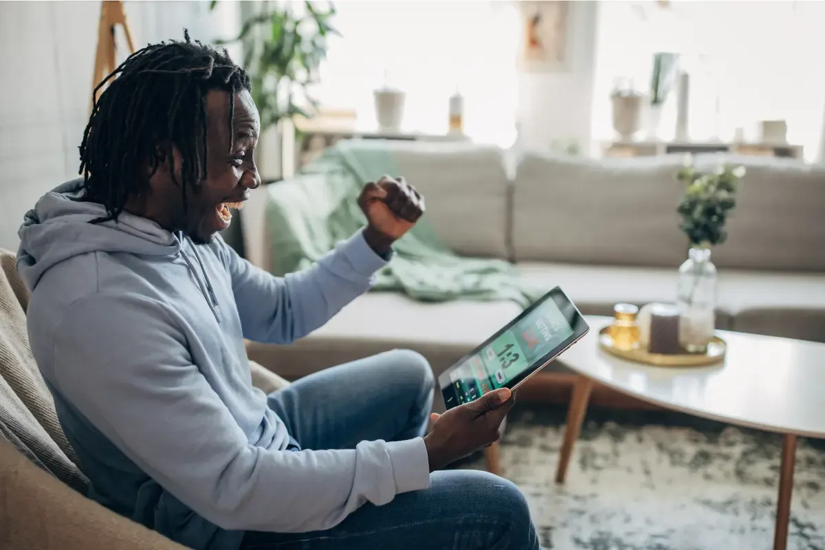 Excited man celebrating a sports bet win while viewing a live score on a tablet