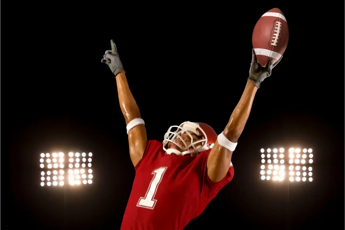 College football celebration as a player in a red jersey catches a football under stadium lights