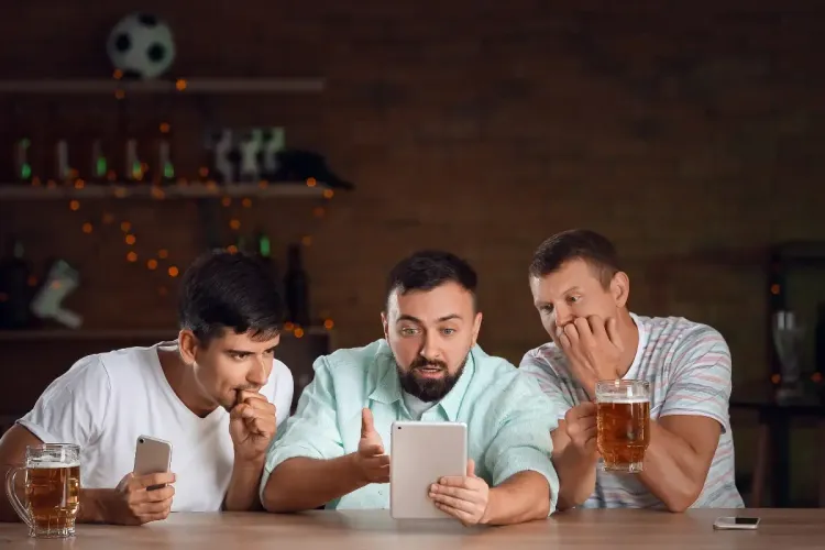 Fantasy basketball strategy as three friends anxiously check their fantasy scores on a tablet at a bar.