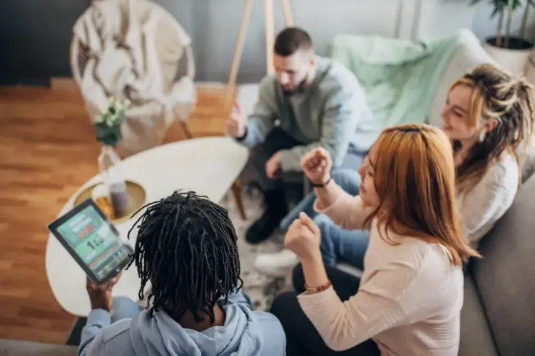 Group of friends cheering while watching sports and tracking scores on a tablet in a cozy living room