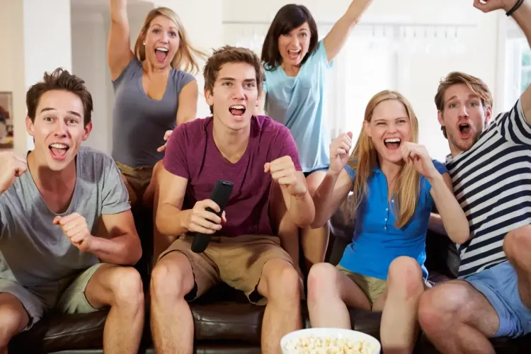 Group of friends enthusiastically cheering while watching TV in a cozy home setting