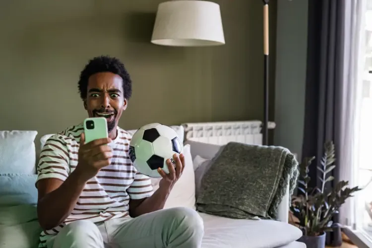 Intense peer-to-peer fantasy sports engagement with a man holding a soccer ball and reacting to his smartphone