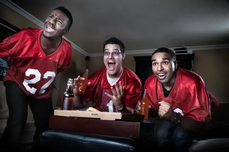 NFL survivor pool fans in red jerseys react emotionally while watching a football game with drinks and pizza